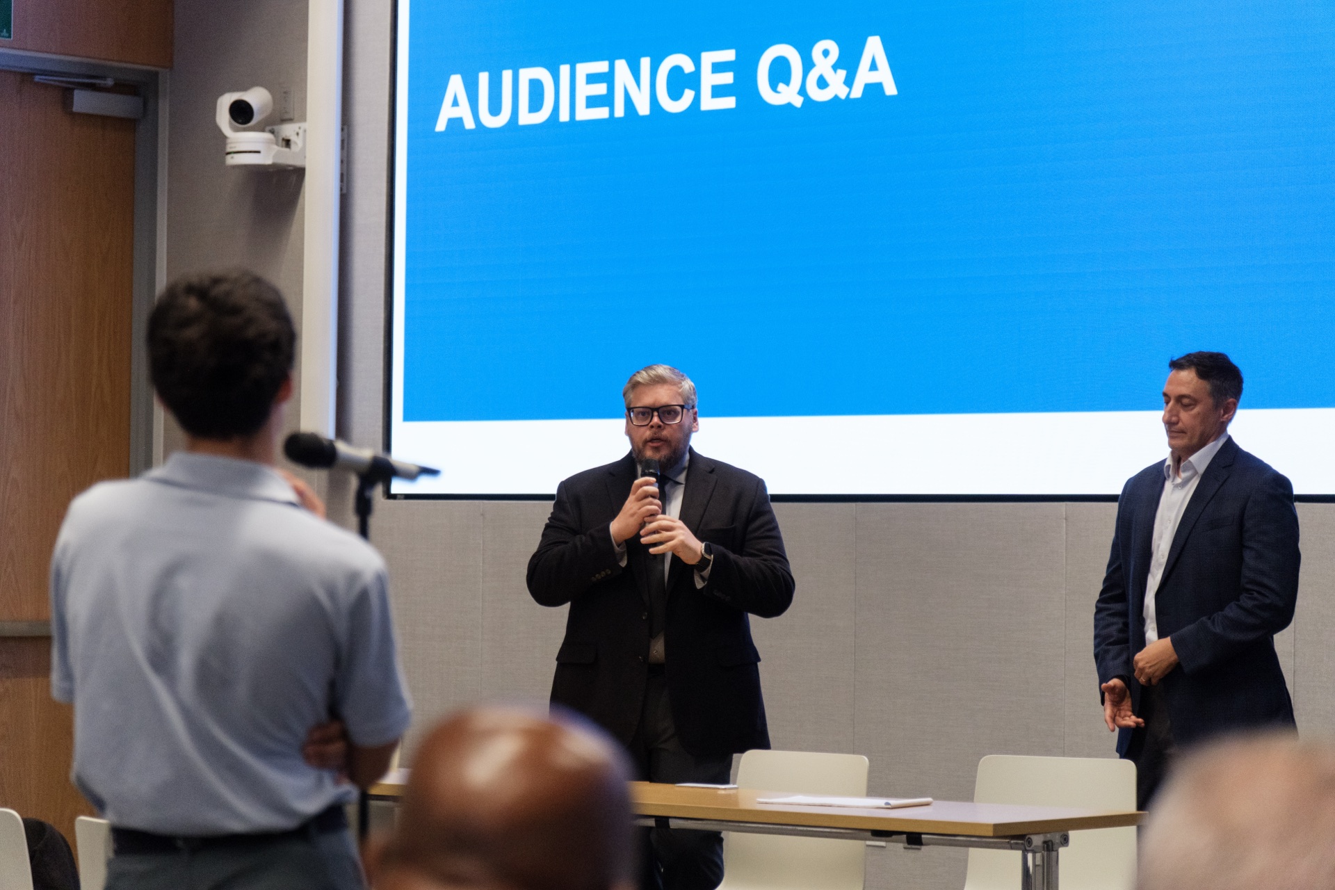 Brad Groux answering an audience question with Giovanni Capriglione beside him during the AI debate.